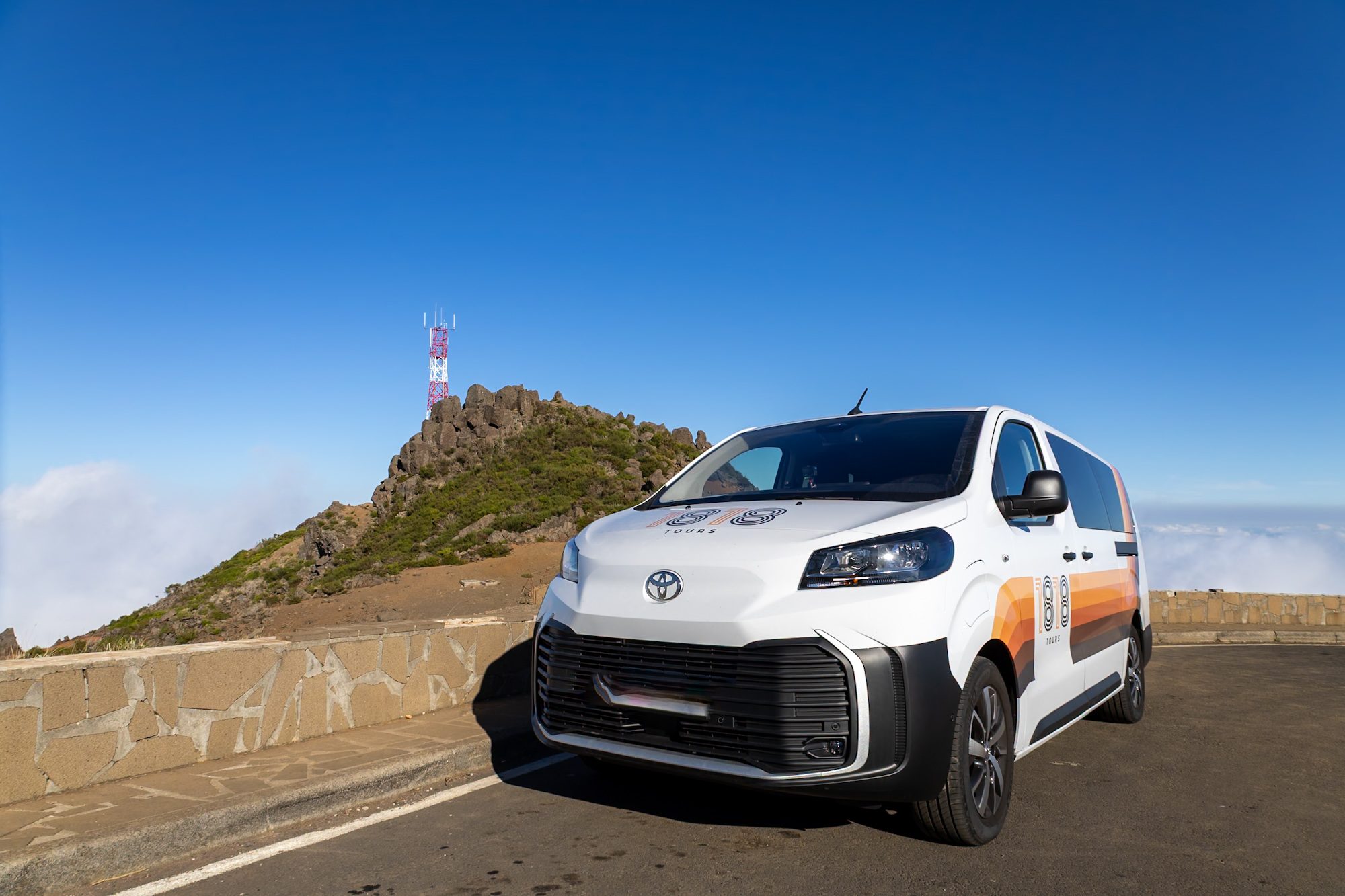 The white 1818 Tours electric van parked at Pico do Areeiro, with the antenna behind