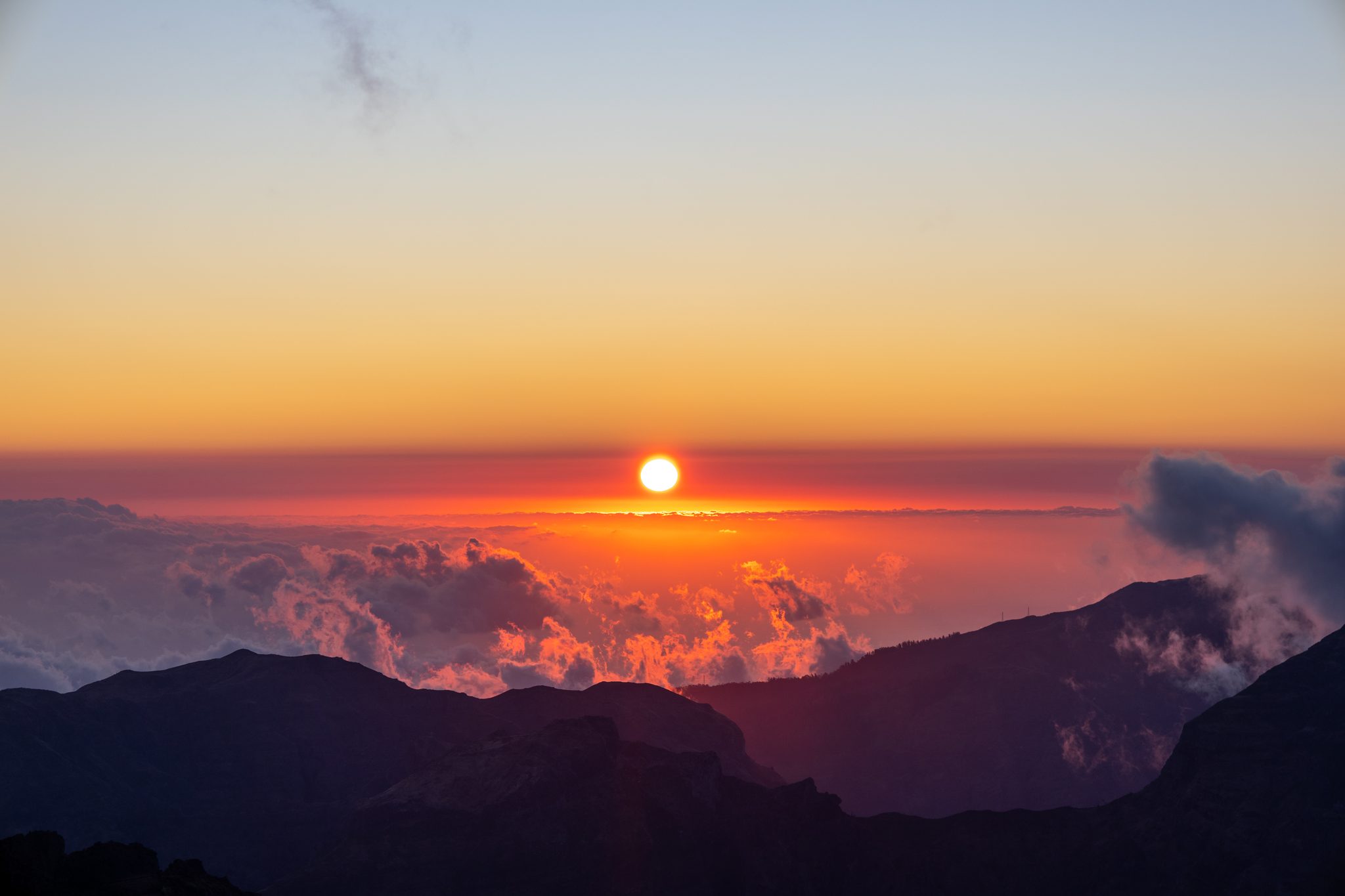 O sol sobre nuvens vermelhas e laranja ao pôr do sol no Pico do Areeiro